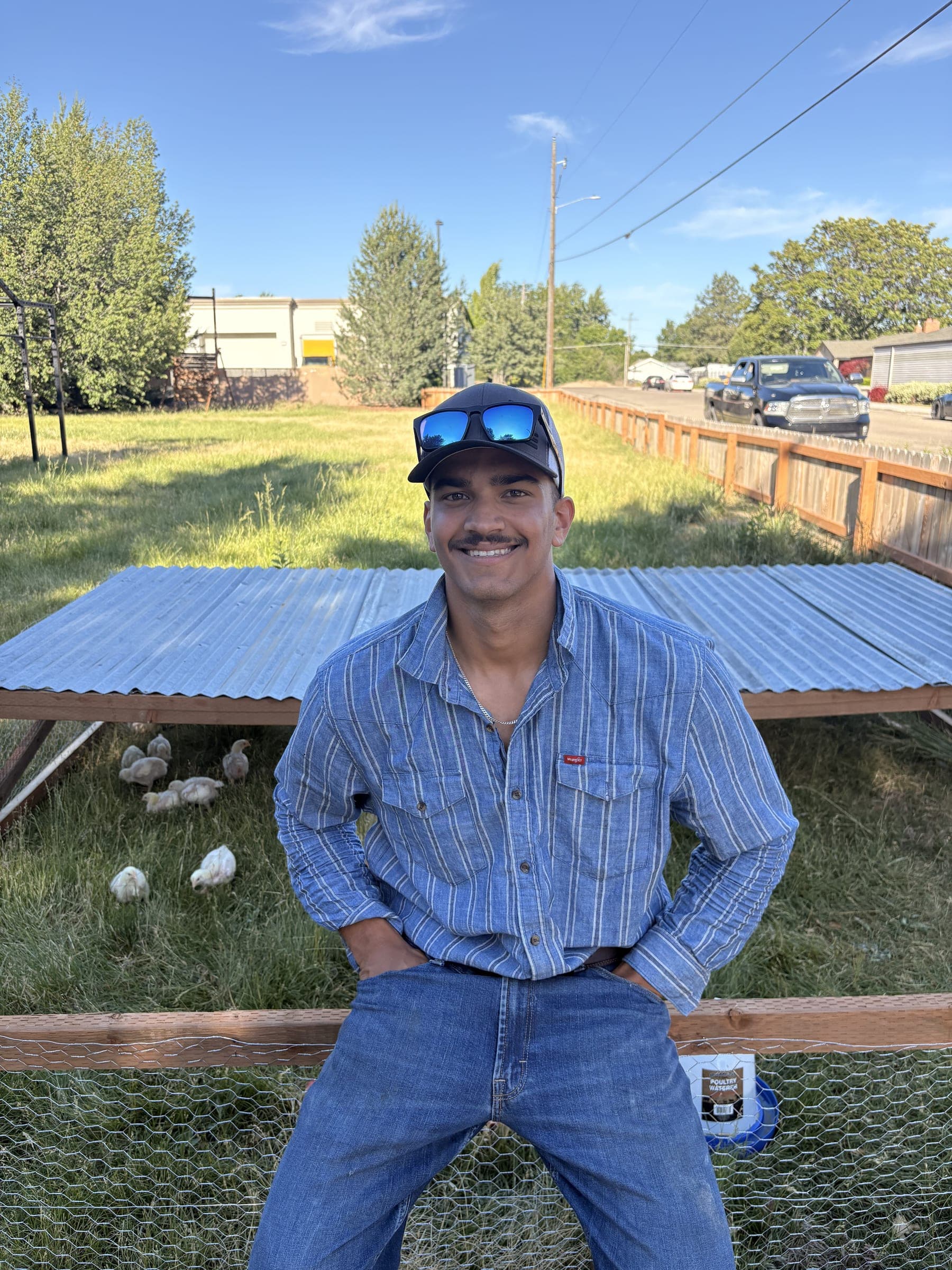 Alex Srinivasan sitting on a chicken tractor with young birds on the grass behind him
